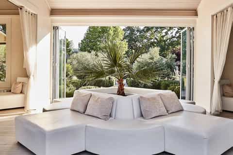 Luxury bedroom with curved white sofa, large windows opening to tropical garden with palm trees
