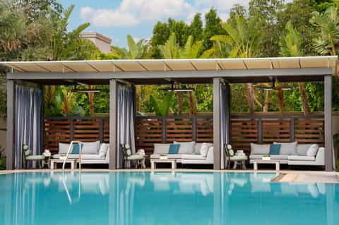 Modern poolside cabanas with white curtains, lounge seating, and tropical plants