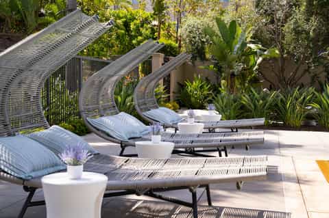 Curved lounge chairs with striped cushions and woven shade structures in a garden courtyard setting