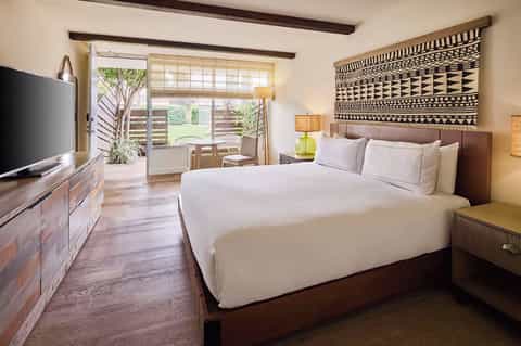 Tropical resort bedroom with king bed, sliding glass doors to patio, wooden beams, and African wall art