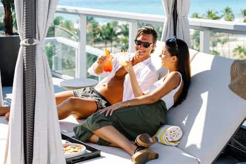 Couple enjoying tropical cocktails on a sunny beachfront terrace with ocean views