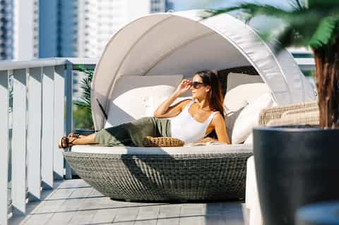 Woman relaxing in white canopy daybed on rooftop terrace with city buildings in background