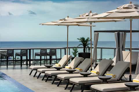 Oceanfront resort deck with loungers under large umbrellas, sea views, and contemporary furniture