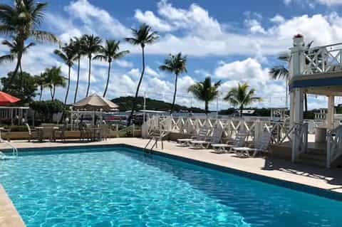 Resort swimming pool with white lounge chairs, palm trees, and covered pavilion structure