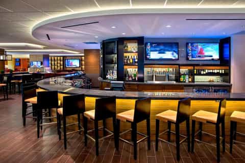 Contemporary hotel bar with curved ceiling, multiple TV screens, and elegant seating