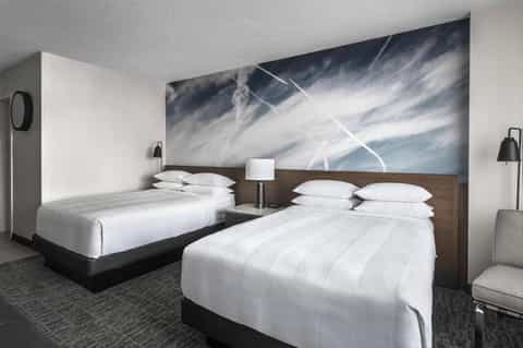 Hotel room with two queen beds, white linens, and abstract sky artwork