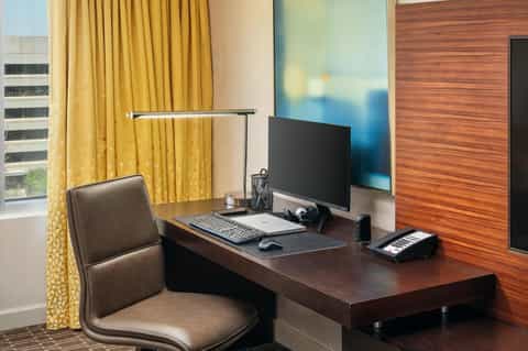 Hotel room workspace with wooden desk, computer monitor, and yellow curtains with ocean view