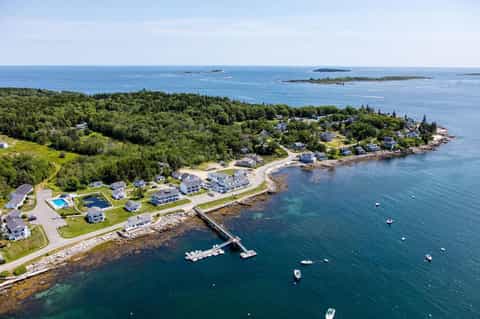 Aerial coastal view of waterfront residential community with dock, boats, and forested peninsula