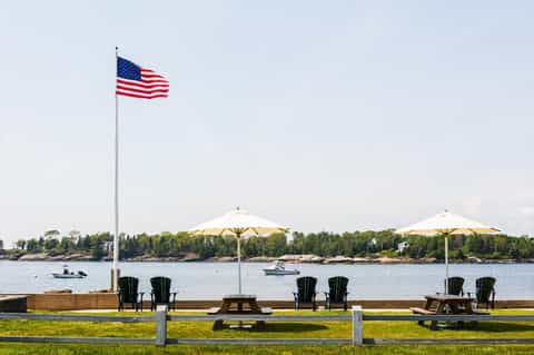 Waterfront picnic area with Adirondack chairs, umbrellas, American flag, and lake views