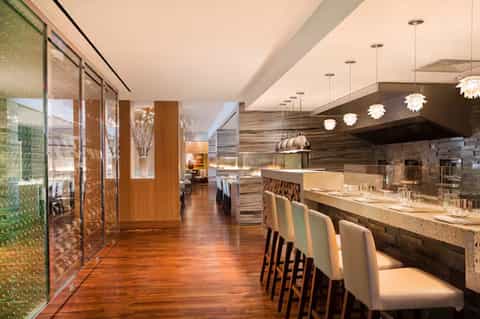 Modern upscale restaurant interior with wooden floors, bar seating, pendant lights, and contemporary design