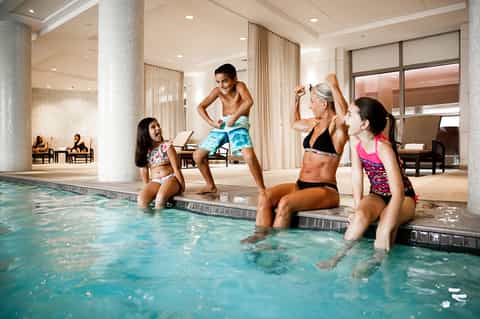 Indoor pool with families enjoying water activities, columns, and lounge seating