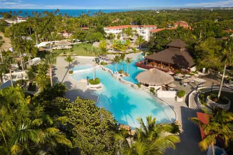 Aerial view of tropical resort with multiple pools, palm trees, and oceanfront setting