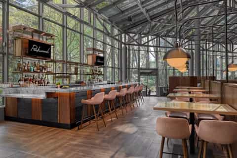 Contemporary glass-enclosed restaurant bar with wooden seating and forest views