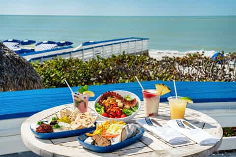 Beachfront dining table with tropical cocktails, seafood platters, and ocean view at sunset