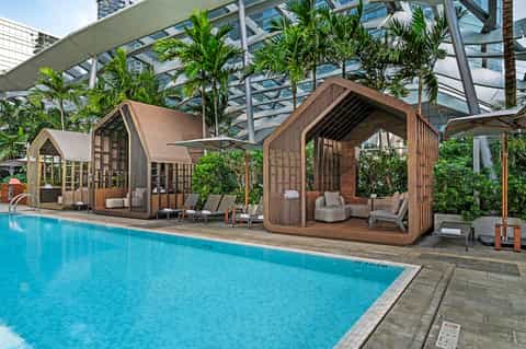 Modern pool area with wooden cabana structures, palm trees, and glass ceiling in contemporary resort setting