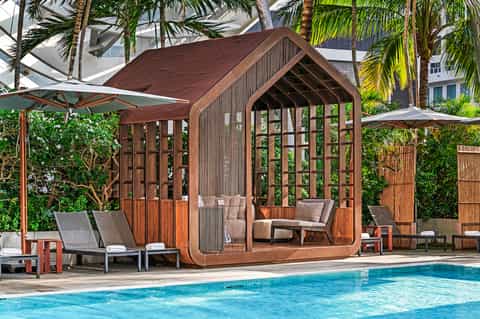 Modern wooden cabana by tropical pool with palm trees, lounge chairs, and umbrellas