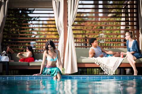 Resort pool with guests relaxing on lounge chairs under pergola with ocean views