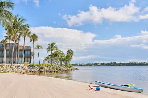 Beachfront resort property with palm trees, sandy beach, kayaks, and calm waterway