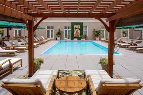 Indoor-outdoor pool surrounded by wooden pergolas, white lounge chairs, and potted plants