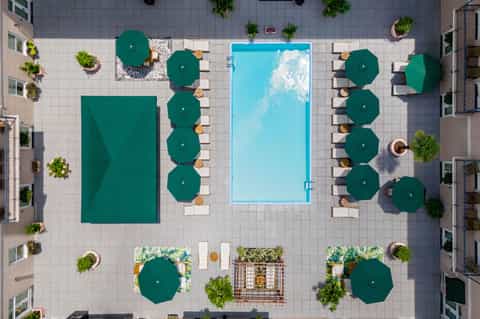Aerial view of resort pool deck with green umbrellas, loungers, and surrounding tropical vegetation