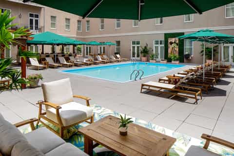 Resort courtyard pool with turquoise water, lounge chairs, and green umbrellas