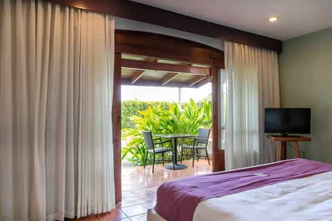 Luxury bedroom with purple bedding, terrace doors opening to ocean view patio with tropical plants
