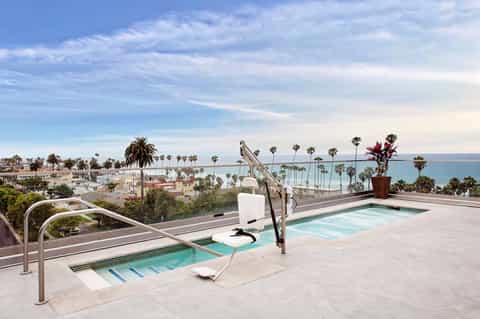Rooftop spa area with hot tubs overlooking palm-lined coastal town and turquoise ocean waters
