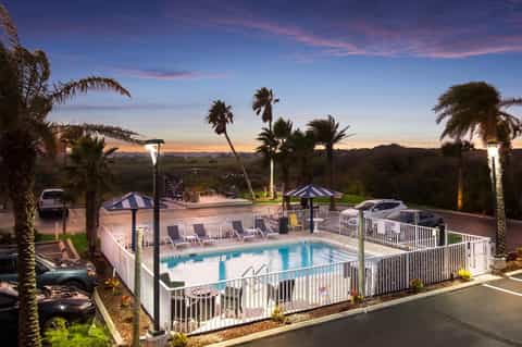 Resort pool at sunset surrounded by palm trees, loungers, and umbrellas overlooking landscape