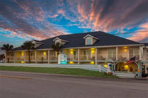 Beachfront hotel with white exterior, palm trees, and lit entryway at sunset with dramatic sky