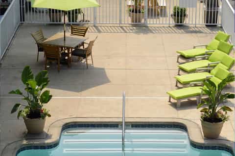 Elevated pool deck with lounge chairs, umbrella, potted plants, and white railings overlooking calm pool water