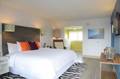 Modern hotel bedroom with queen bed, colorful pillows, and contemporary furnishings