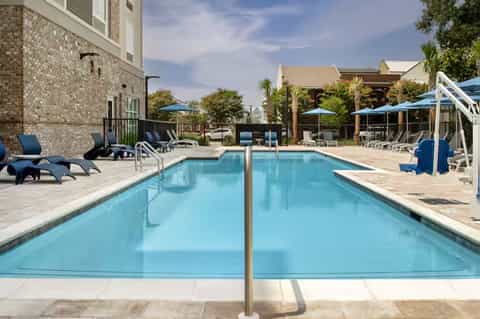 Resort lap pool with clear water, lounge chairs, umbrellas, and brick building