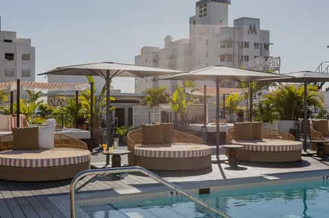 Rooftop pool deck with curved lounge seating, umbrellas, and striped cushions overlooking historic buildings