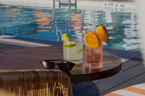 Refreshing cocktails with lime and orange garnish on wooden table by the pool
