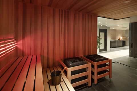 Modern sauna interior with red wooden walls, benches, and glass shower area with warm lighting