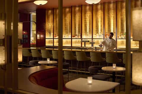 Upscale bar lounge with gold-lit wall display, modern seating, and bartender in white shirt