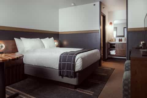 Contemporary hotel bedroom with white bedding, dark wood accents, and ensuite bathroom