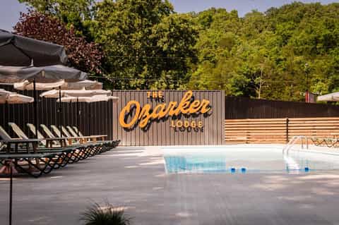 The Oakslee Lodge pool area surrounded by trees with lounge chairs and umbrellas on concrete deck