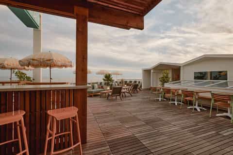 Beachfront resort deck with wooden bar, thatched umbrellas, lounge seating, and ocean horizon view