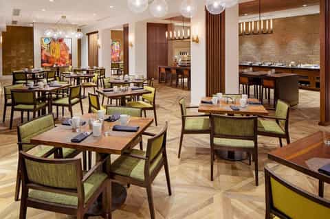 Modern dining room with wood tables, green chairs, and brick accent wall with pendant lighting