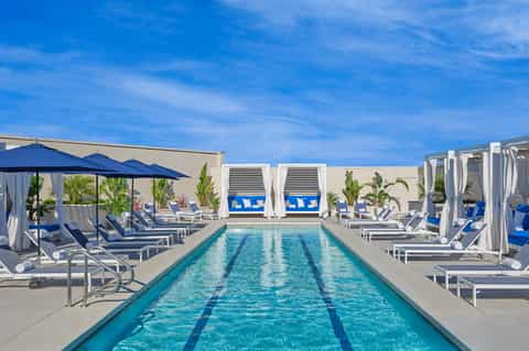 Olympic-length lap pool with blue loungers, white cabanas, umbrellas, and clear blue sky at a luxury resort