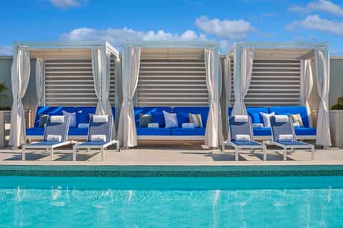Luxury poolside cabanas with blue cushions and white curtains overlooking turquoise water