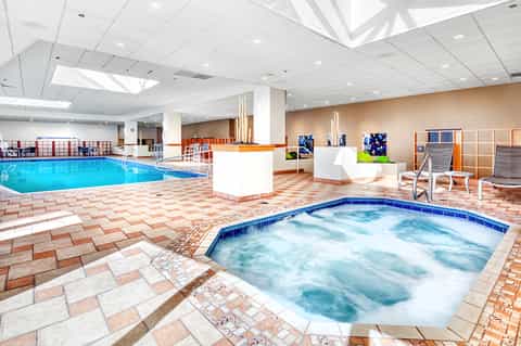 Indoor aquatic center with large swimming pool, hot tub, and relaxation seating areas under skylights