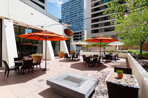 Rooftop terrace with orange umbrellas, dining tables, fire pit, and urban skyline views