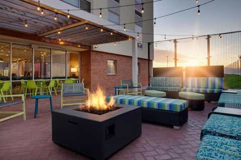 Rooftop terrace with fire pit, colorful striped seating, and brick building at golden hour