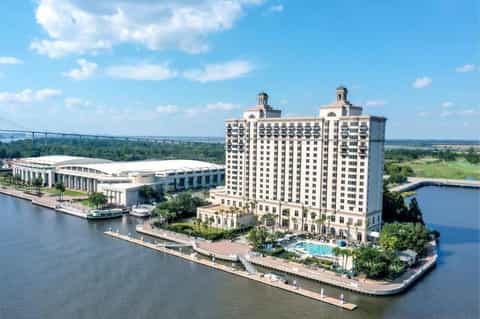 Waterfront hotel tower with classical architecture on riverbank, featuring white convention center and manicured grounds