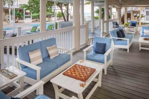 Coastal resort deck with blue and white lounge chairs, chess board, and ocean views through columns