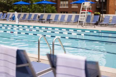 Olympic-sized swimming pool with lane dividers, lifeguard stand, blue umbrellas, and lounge chairs