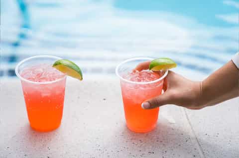 Two coral-colored cocktails with lime garnish by pool overlooking ocean