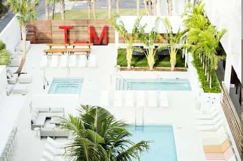 Aerial view of modern resort with palm trees, multiple pools, and red TM signage